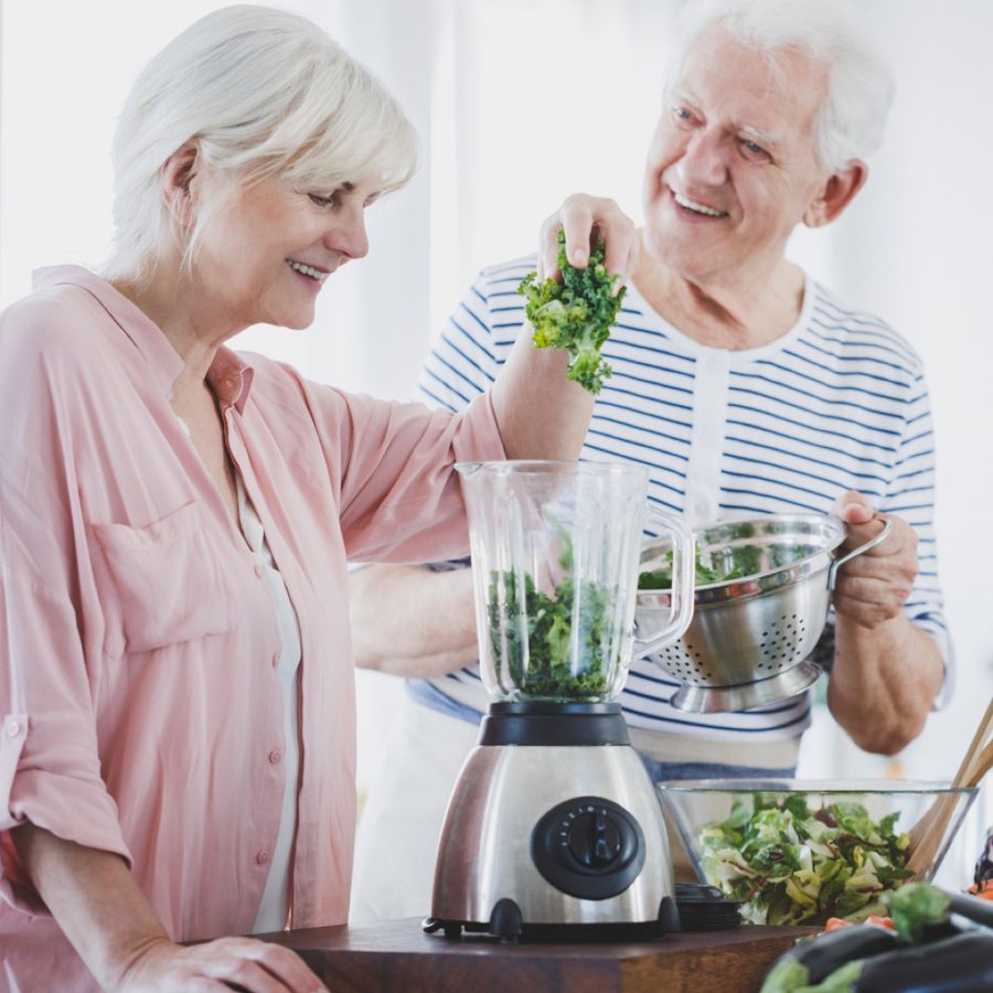 A senior woman and man making a smoothie together at the kitchen counter