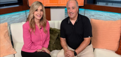 Two people sit on a newsroom set.