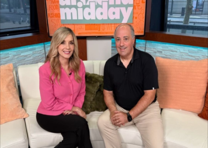 Two people sit on a newsroom set.